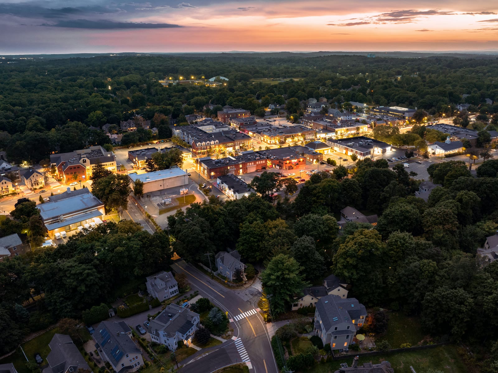 A small town at dusk from the air, its lights coming on beneath a passing storm front